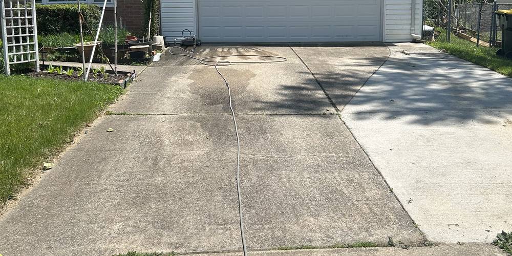 A driveway photographed mid-job: the right side already cleaned bright, the left side still grey with the hose on it